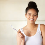 Young black girl in a white tanktop smiles while holding a toothbrush