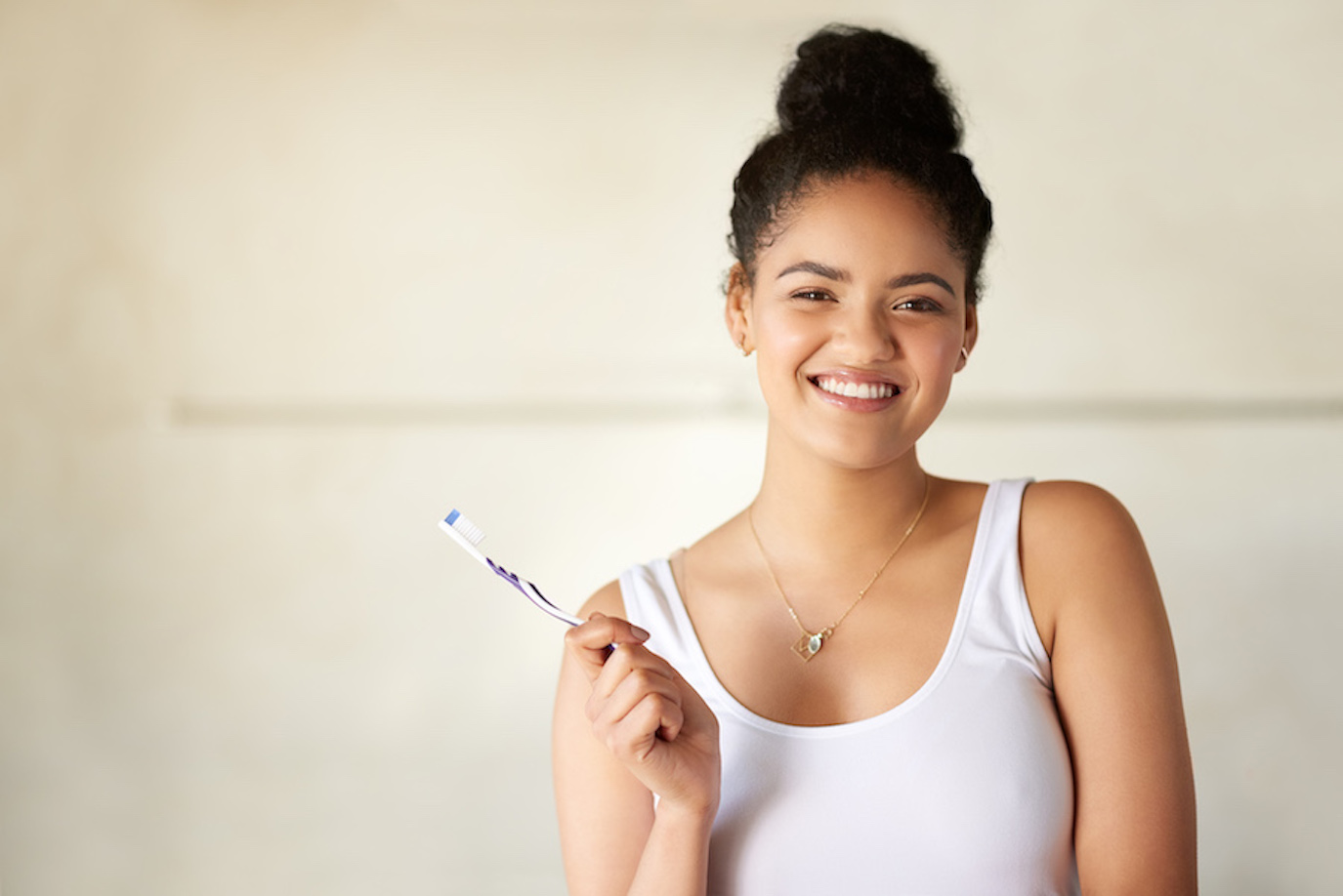 Young black girl in a white tanktop smiles while holding a toothbrush