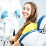 Brunette young woman in a yellow shirt smiles as she sits in a dental chair