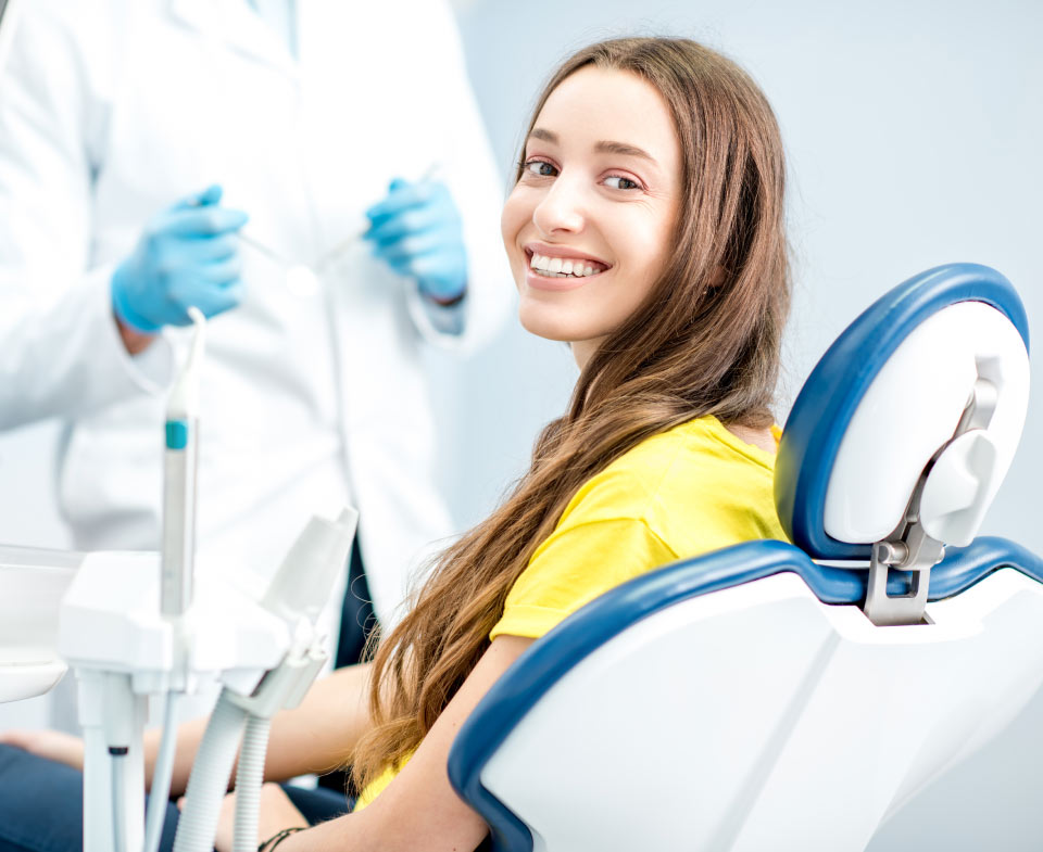 Brunette young woman in a yellow shirt smiles as she sits in a dental chair