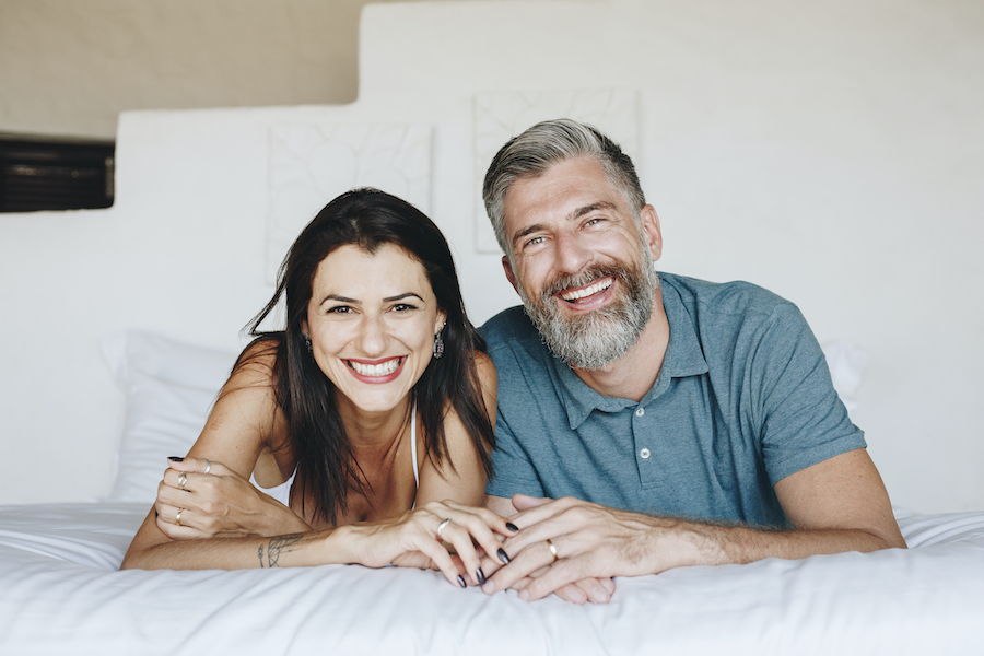 Brunette woman and man with salt and pepper hair smile with teeth improved with dental restorations